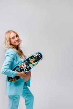 a pregnant girl in turquoise clothes with a skateboard in her hands on a gray background.