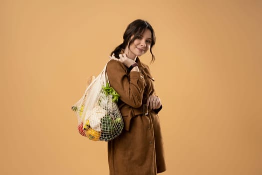 Beautiful young woman holding mesh grocery bag with vegetables. Zero waste, plastic free. Eco friendly concept. Sustainable lifestyle