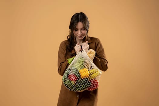 Beautiful young happy brunette woman in dress holding mesh grocery bag with vegetables. Zero waste, plastic free. Eco friendly concept. Sustainable lifestyle