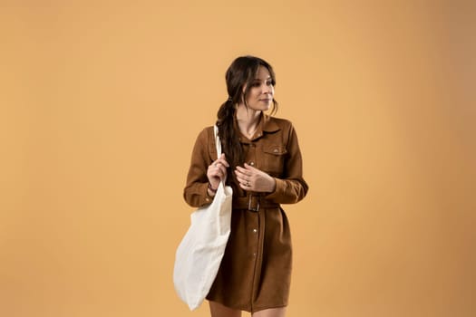 Brunette young smiling girl wearing dress with a white blank cotton bag. Mock-up of blank bag