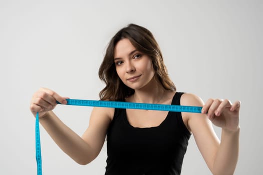 Slim young beautiful brunette girl in black underwear with a measuring tape in front of her face. Photo of beautiful brunette girl with perfect body. Fitness or body care concept