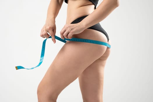 Healthy, sport and fitness lifestyles concept. Young woman in black underwear is measuring her thigh with measuring tape on white background