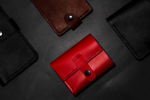 A set of handmade leather wallets. Black, brown, red. Leather craft. Men's wallets on a dark background. View from above.