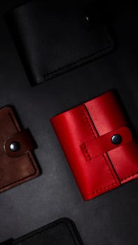 A set of handmade leather wallets. Black, brown, red. Leather craft. Men's wallets on a dark background. View from above.