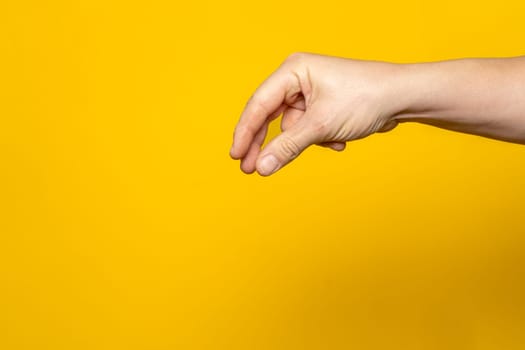 Tough man's hand making the gesture of picking up an object from above isolated on yellow background