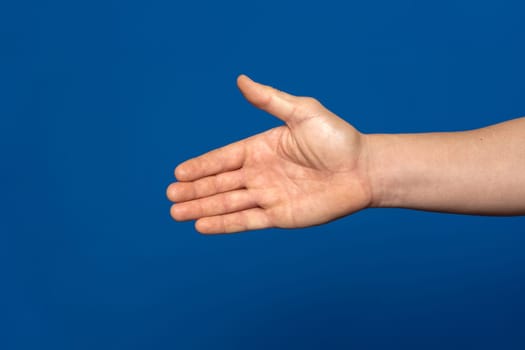 Man stretching out his hand to handshake isolated on a blue background. Man's hand ready for handshake. Formal greeting, gesture of introduction and respect towards someone