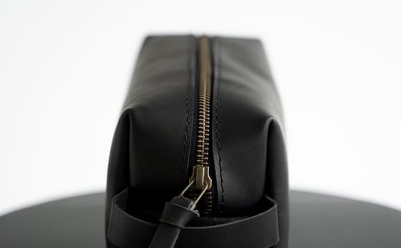 Close up black leather classic mens cosmetic bag with a metal gold zip on a black chair with a white background