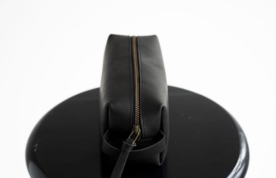 Black leather classic mens cosmetic bag with a metal gold zip on a black chair with a white background