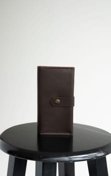 New brown genuine leather wallet on a wooden black chair with white background. Men's accessories