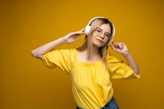 Lifestyle Concept. Portrait of beautiful woman in a glasses and yellow shirt joyful listening to music. Yellow studio background. Copy Space