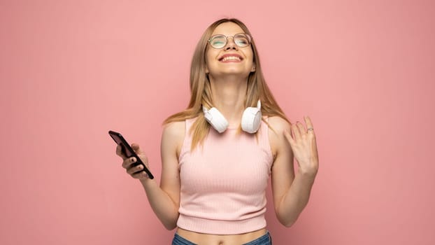 Closeup photo of attractive positive laughing young blonde woman wearing stylish yellow shirt and glasses communicating on mobile phone and smiling isolated over yellow background