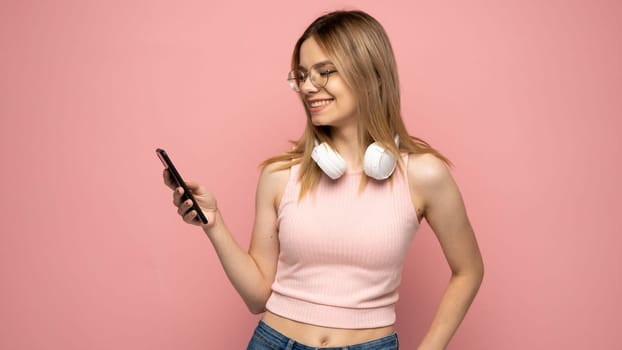 Young blonde woman in a glasses and pink t-shirt over isolated pink background sending a message with the mobile