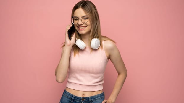 Surprised young happy girl in pink t-shirt using mobile phone, typing sms message isolated on pink background, studio portrait. People lifestyle concept. Mock up copy space