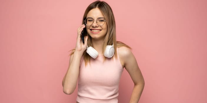 Portrait of a cute happy girl in yellow shirt and glasses with a headphones on a neck talking on mobile phone and laughing