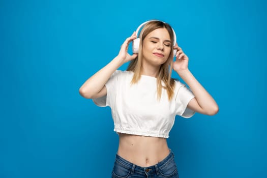 Beautiful young woman in headphones listening to music blue background. Young beautiful woman in bright outfit enjoying a music