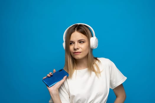 Happy young blonde woman in a white t-shirt dancing to the music she is listening to on her phone