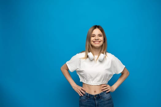 Beautiful young blonde woman with headphones and mobile device listening to music and smiling and dancing, isolated on blue background