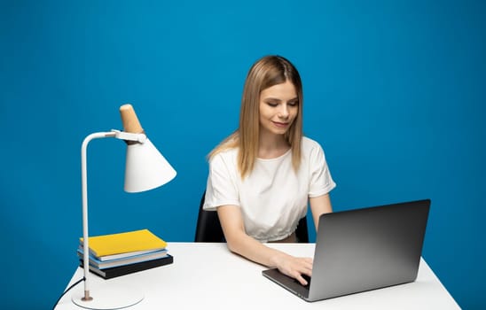 Portrait of a pretty young woman studying while sitting at the table with grey laptop computer, notebook. Smiling business woman working with a laptop isolated on a grey background