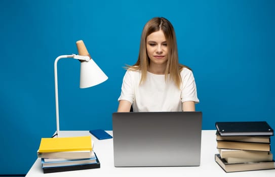 Portrait of a pretty young woman studying while sitting at the table with grey laptop computer, notebook. Smiling business woman working with a laptop isolated on a grey background