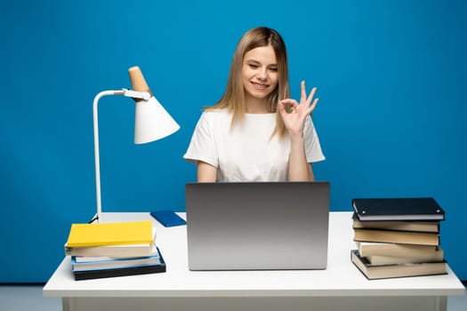 Happy woman using laptop and showing ok sign to a friends, colleagues or to a clients that everything is ok and looking in a computer screen