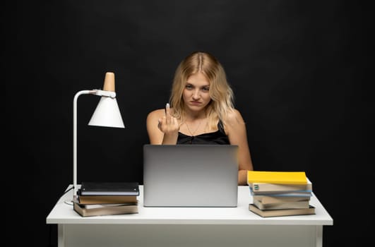 Portrait of young woman sitting at the table and showing middle finger in a laptop