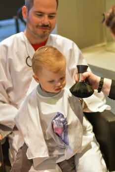 Dad holds a little boy of a one years old at the hairdresser for a first haircut