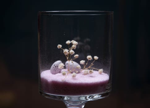 A glass with Easter eggs on pink sand background, holiday decoration. High quality photo