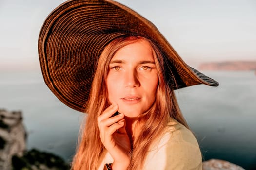 Portrait of happy young woman wearing summer black hat with large brim at beach on sunset. Closeup face of attractive girl with black straw hat. Happy young woman smiling and looking at camera at sea