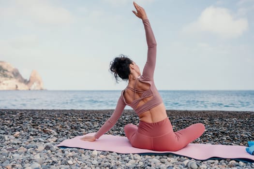 Middle aged well looking woman with black hair doing Pilates with the ring on the yoga mat near the sea on the pebble beach. Female fitness yoga concept. Healthy lifestyle, harmony and meditation.