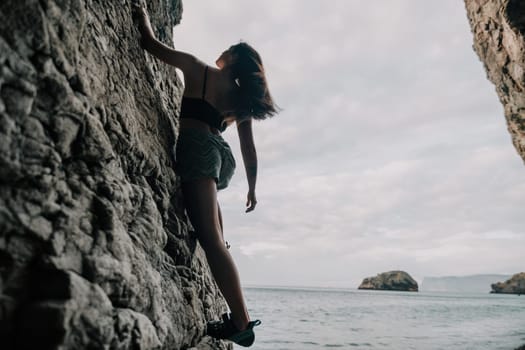 A girl climbs a rock. The athlete trains in nature. Woman overcomes difficult climbing route. Extreme hobby. Tourist woman rock climber hiking on mountains rocks over beautiful sea coast