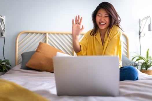 Asian young woman in video call taking online classes. Greeting classmates. Waving hand towards laptop. Chinese teen girl video call. E-learning concept. Video call concept.