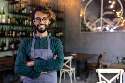 Happy waiter wearing apron standing in bar with arms crossed looking at camera. Copy space. Restaurant concept.