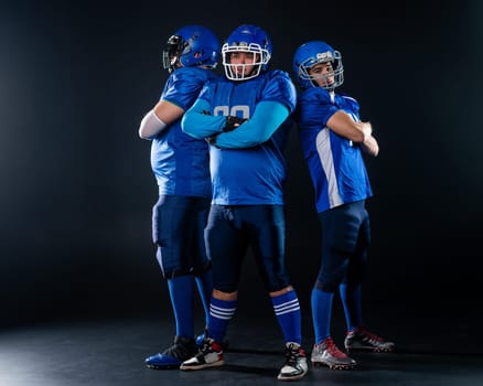 Portrait of three men in blue American football uniforms standing with their arms crossed over their chests on a black background