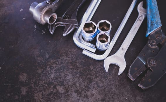 Hand tools consisting of wrenches, pliers, socket wrenches, laid out on old steel plate background.