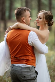 young couple bride in a white short dress and groom in a gray suit in a pine forest among the trees