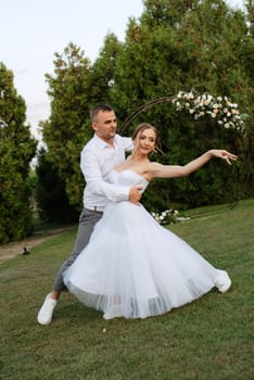 the first dance of the groom and bride in a short wedding dress on a green meadow