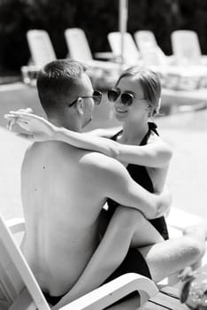 guy and a girl in bathing suits are relaxing, sunbathing and having fun near the blue pool