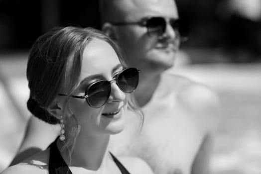 guy and a girl in bathing suits are relaxing, sunbathing and having fun near the blue pool