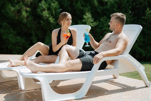 guy and a girl in bathing suits are relaxing, sunbathing and having fun near the blue pool