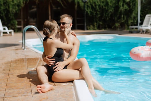 guy and a girl in bathing suits are relaxing, sunbathing and having fun near the blue pool