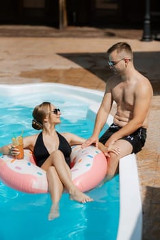 guy and a girl in bathing suits are relaxing, sunbathing and having fun near the blue pool