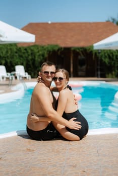 guy and a girl in bathing suits are relaxing, sunbathing and having fun near the blue pool