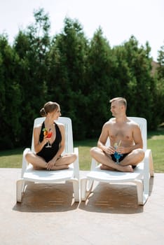 guy and a girl in bathing suits are relaxing, sunbathing and having fun near the blue pool