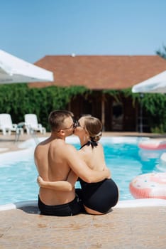 guy and a girl in bathing suits are relaxing, sunbathing and having fun near the blue pool