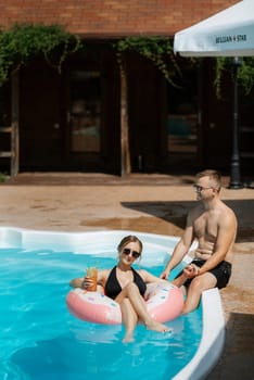 guy and a girl in bathing suits are relaxing, sunbathing and having fun near the blue pool