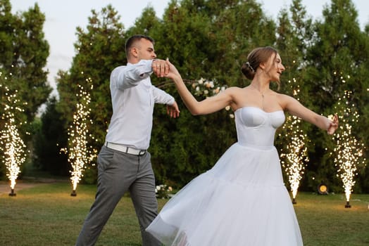 the first dance of the groom and bride in a short wedding dress on a green meadow