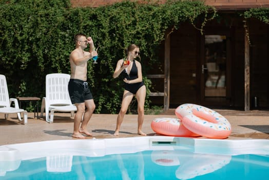 guy and a girl in bathing suits are relaxing, sunbathing and having fun near the blue pool