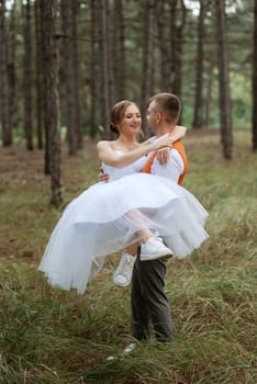 young couple bride in a white short dress and groom in a gray suit in a pine forest among the trees