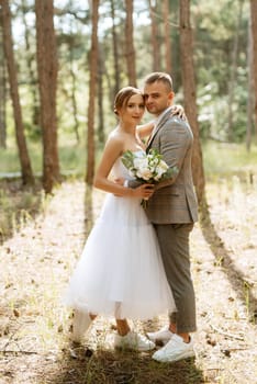 young couple bride in a white short dress and groom in a gray suit in a pine forest among the trees