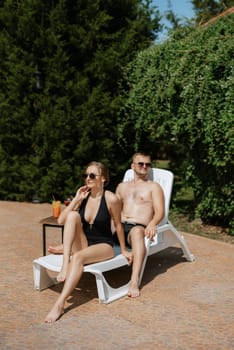 guy and a girl in bathing suits are relaxing, sunbathing and having fun near the blue pool